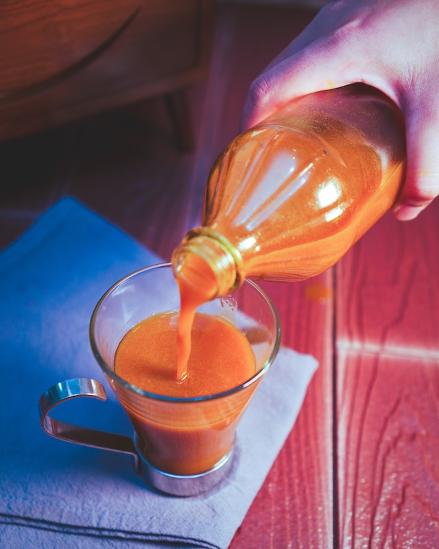 a hand pouring jamu (turmeric and ginger tonig) into a glass